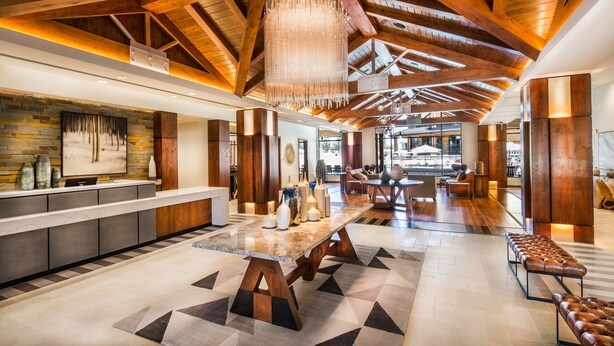 Eine großzügige Lobby mit hoher Decke, Holzbalken, einem zentralen Tisch und Sitzbereichen.