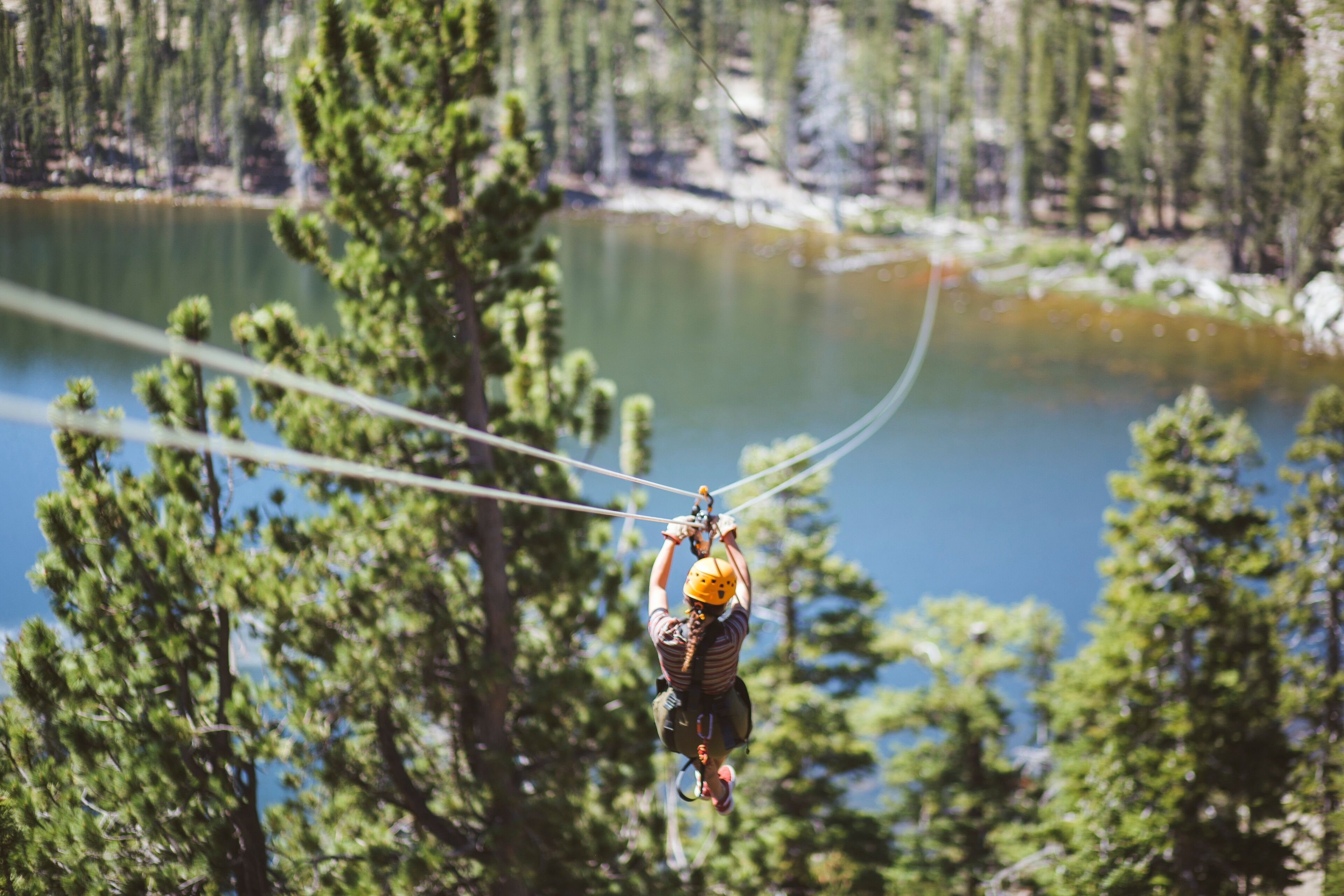 Eine Person zipline durch einen Wald, im Hintergrund ist ein See zu sehen.