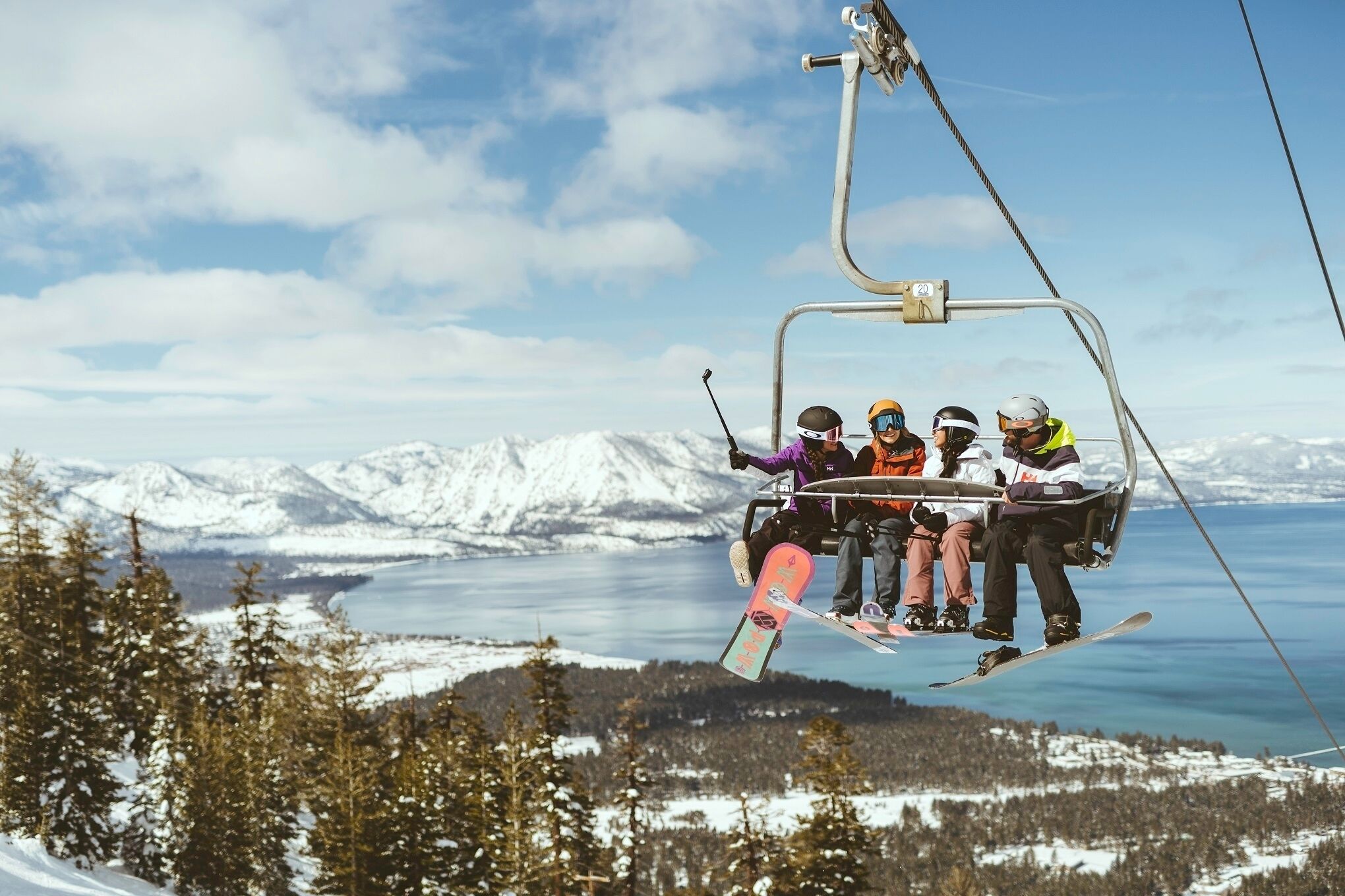 A ski lift with passengers, snow-covered mountains, and a lake in the background.