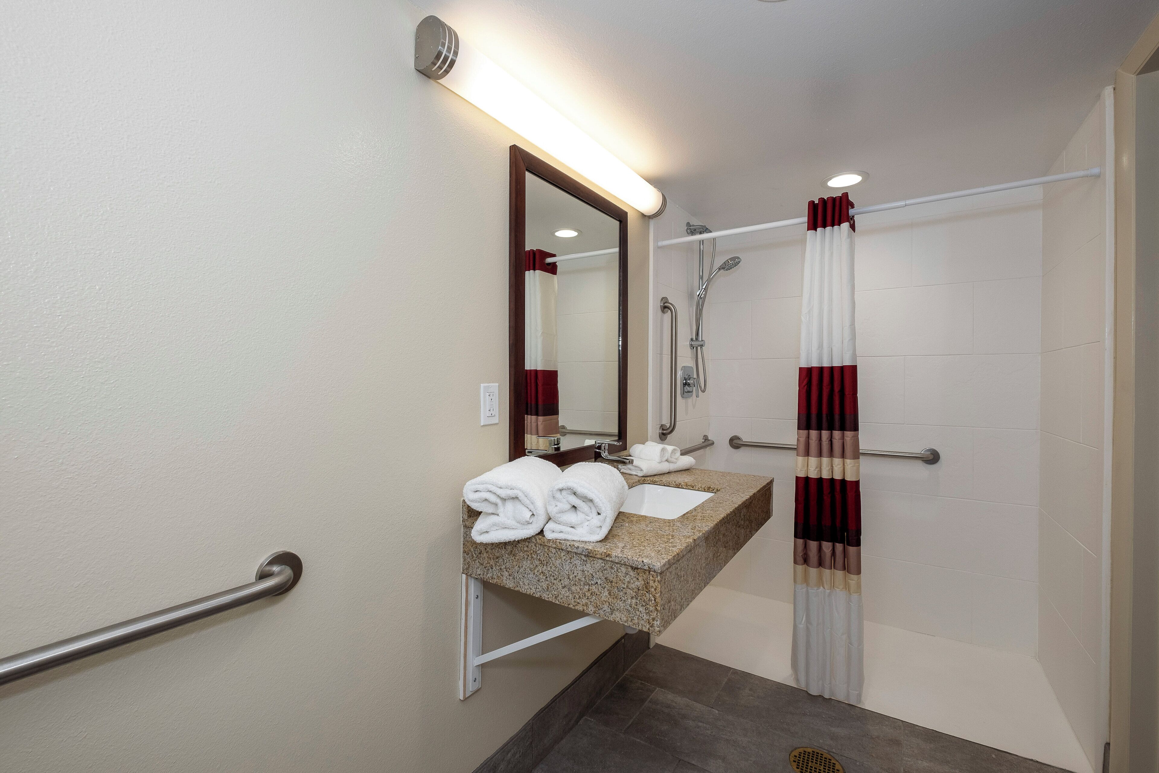 A bathroom with a sink, mirror, towel rack, shower, and grab bars.