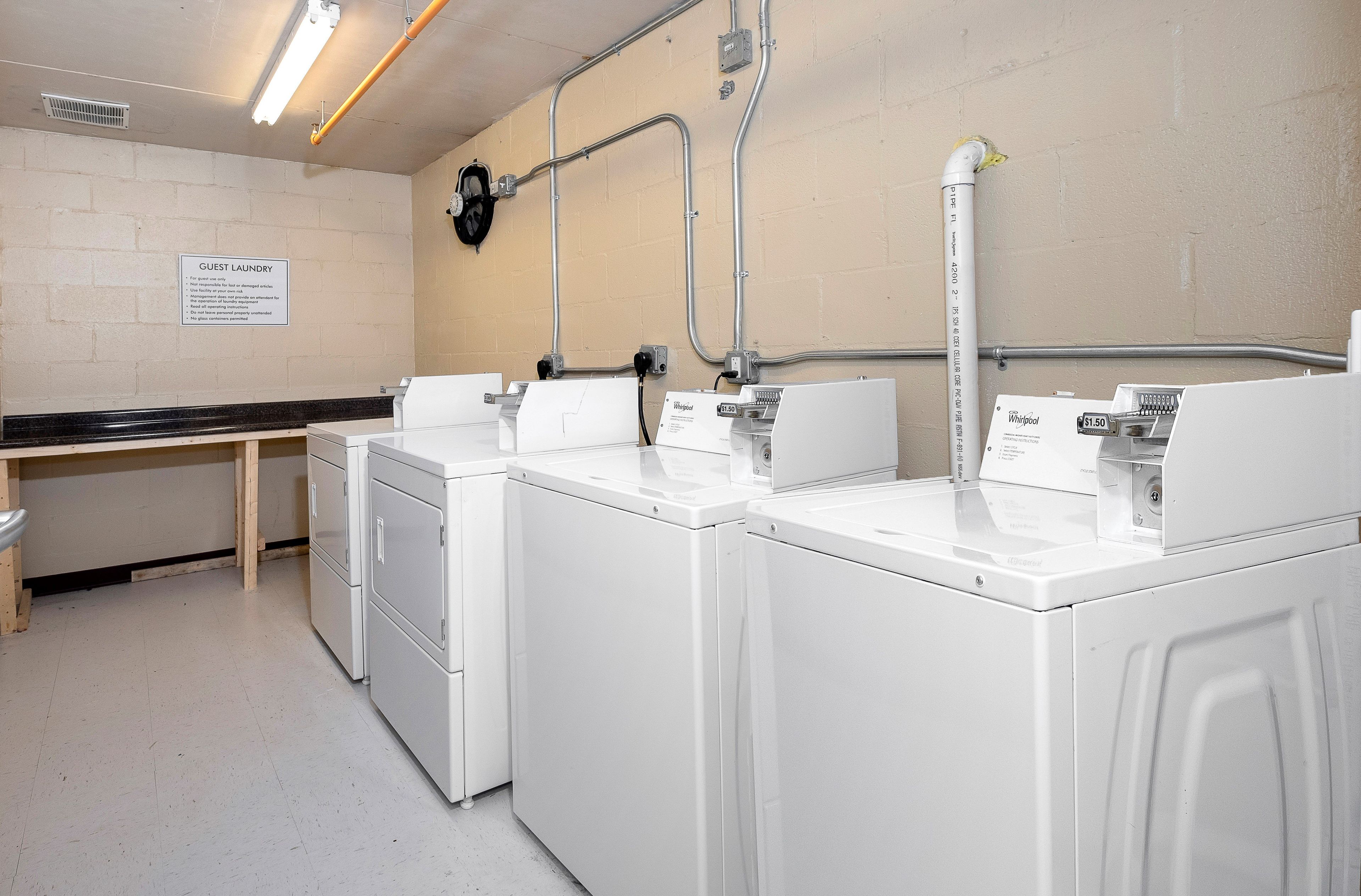 A laundry facility with three white washers and dryers, a bench, and a sign indicating guest laundry services.
