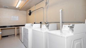 A laundry facility with three white washers and dryers, a bench, and a sign indicating guest laundry services.