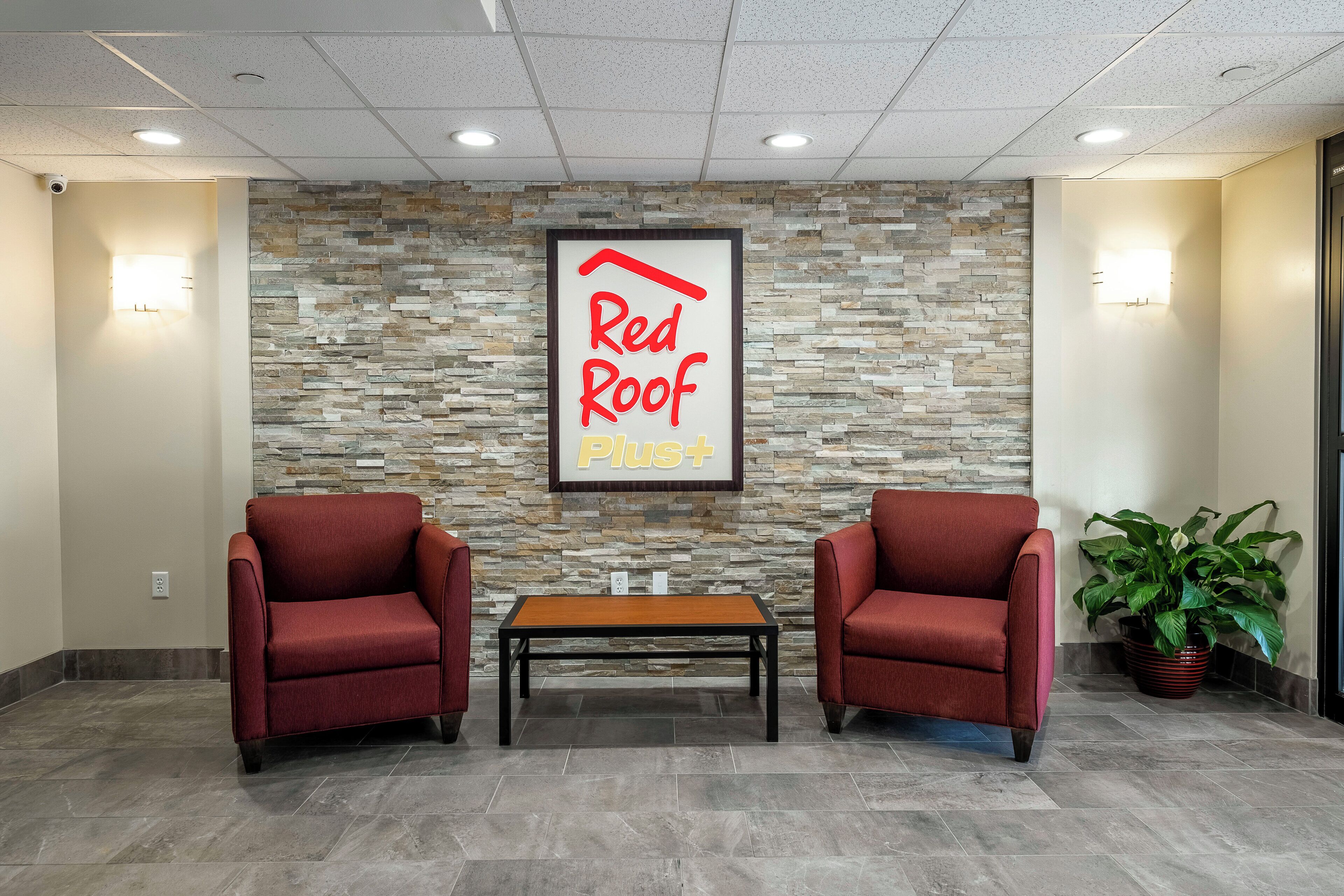 A reception area with a stone wall, two red chairs, a wooden table, and a potted plant.