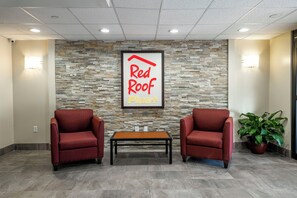 A reception area with a stone wall, two red chairs, a wooden table, and a potted plant. - Red Roof Inn PLUS+ Tuscaloosa - University (Tuscaloosa)
