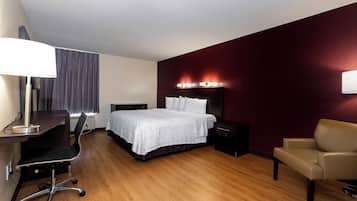 A hotel room with a bed, desk, chair, and a bedside table.
