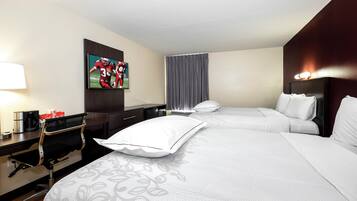 Una habitación de hotel con cama, escritorio con cafetera, televisor en la pared y ventana con cortinas.