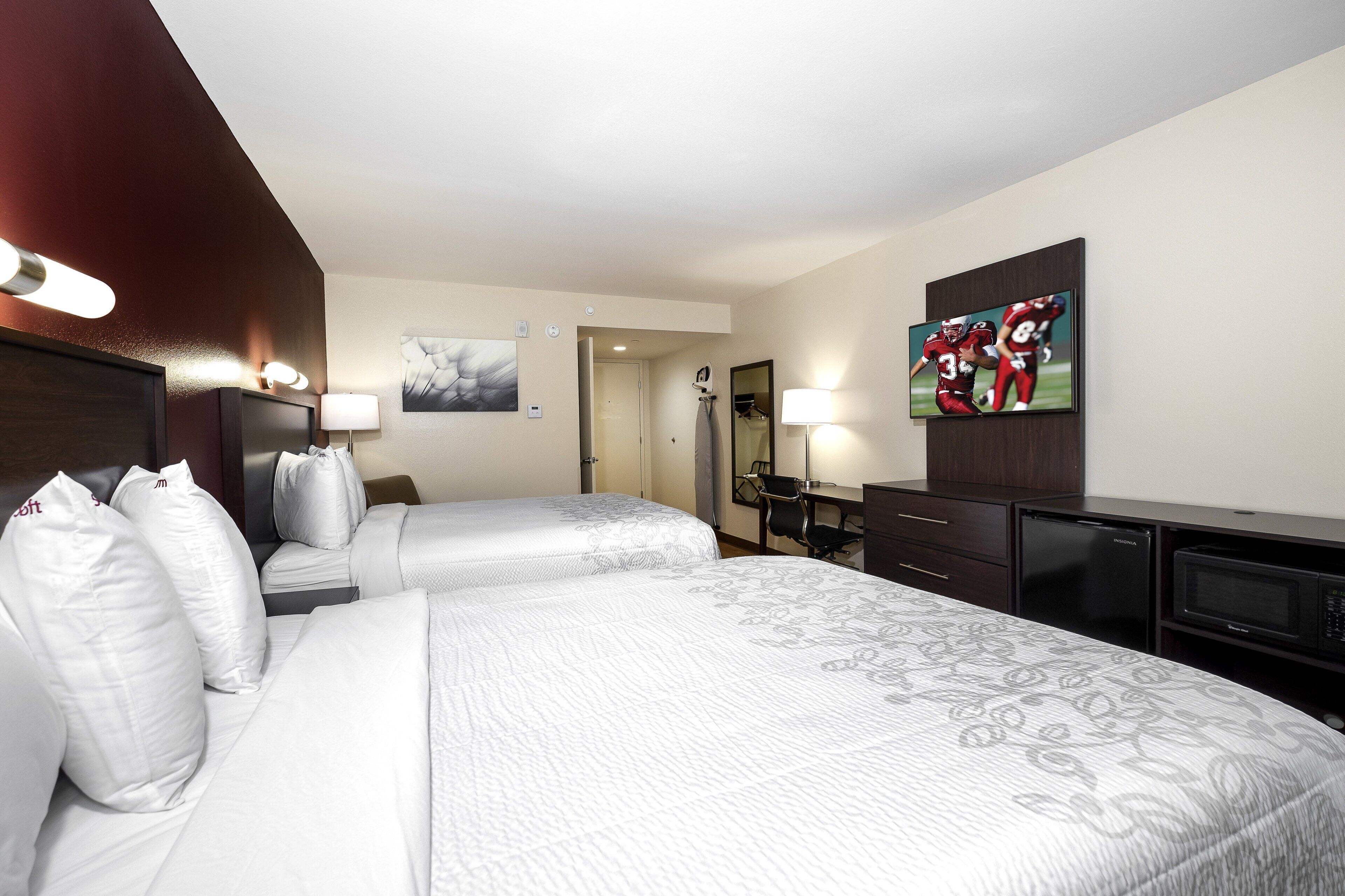 Een hotelkamer met twee bedden, een bureau, een televisie en een minibar.