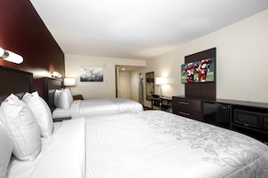 A hotel room with two beds, a desk, a television, and a minibar.