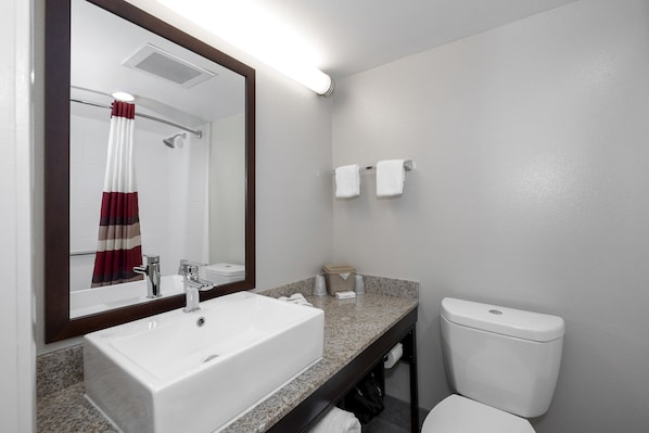 A bathroom with a white sink, a mirror, a shower curtain, and a toilet. - Red Roof Inn PLUS+ Tuscaloosa - University (Tuscaloosa)