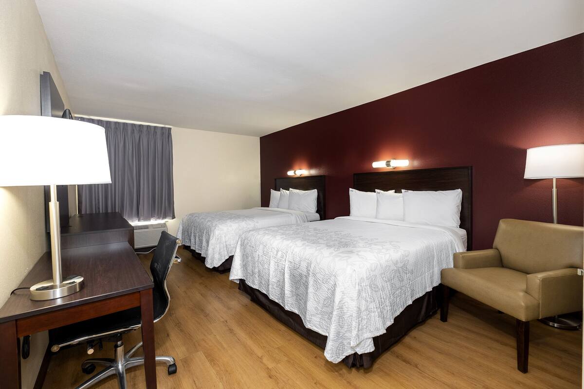 A hotel room with two beds, a desk, a chair, and a desk lamp.