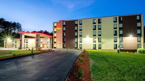 A multi-story hotel with a flat roof, a parking lot, and a well-maintained lawn.
