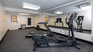 A fitness center with exercise equipment, a mirrored wall, and a door leading to another room. - Red Roof Inn PLUS+ Tuscaloosa - University (Tuscaloosa)