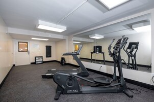 A fitness center with exercise equipment, a mirrored wall, and a door leading to another room.