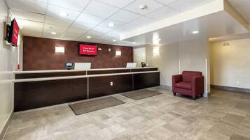 A reception area with a dark wood reception desk, a red chair, a 'Free Wi-Fi All Rooms' sign, and a tiled floor.