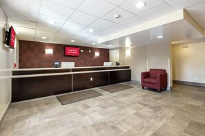 A reception area with a dark wood reception desk, a red chair, a 'Free Wi-Fi All Rooms' sign, and a tiled floor. - Red Roof Inn PLUS+ Tuscaloosa - University (Tuscaloosa)