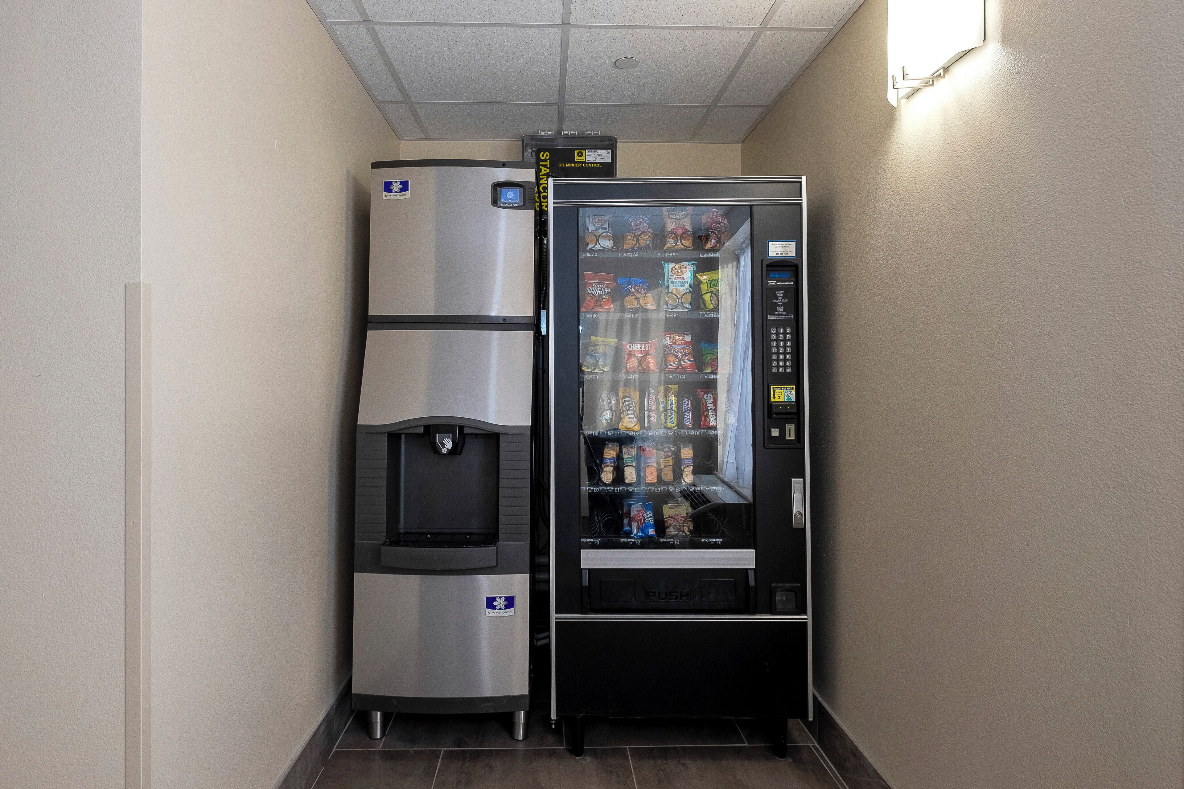 A vending machine with snacks and a water dispenser, located in a hallway with a tiled floor.