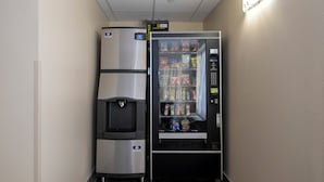 A vending machine with snacks and a water dispenser, located in a hallway with a tiled floor.
