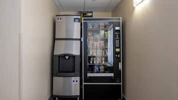 A vending machine with snacks and a water dispenser, located in a hallway with a tiled floor.