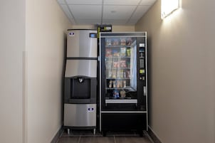A vending machine with snacks and a water dispenser, located in a hallway with a tiled floor.