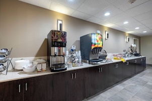 A hotel kitchen with multiple coffee machines, a buffet counter, and various food items.