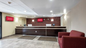 A reception area with a counter, two red chairs, a flat-screen TV, and a sign stating 'Free Wi-Fi All Rooms'. - Red Roof Inn PLUS+ Tuscaloosa - University (Tuscaloosa)