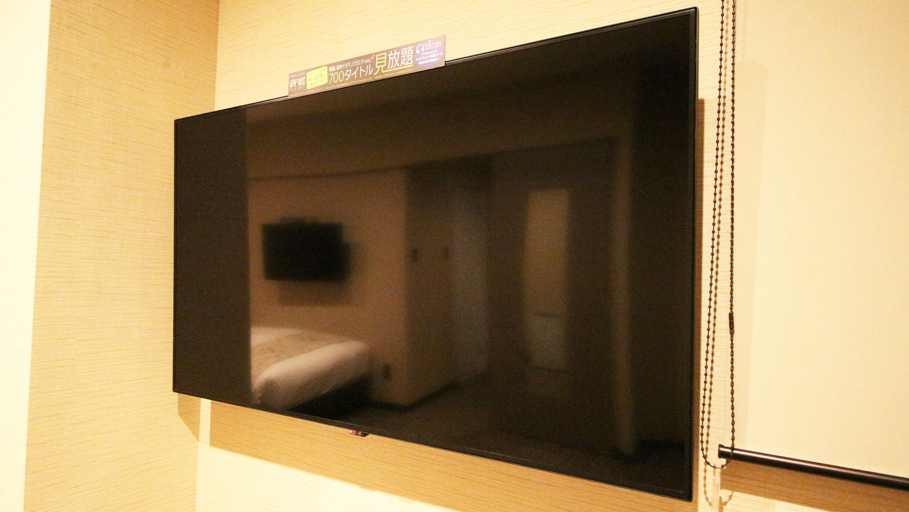 Quarto com uma cama, mesa de cabeceira e televisão na parede.