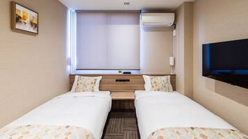 A hotel room with two beds, a TV, an air conditioning unit, and a window with blinds.