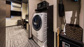 A hotel room with a washing machine, a flat-screen TV, a small desk, and a seating area.