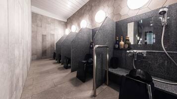 Un baño moderno con encimeras de granito, lavamanos negros y un espejo con cabezal de ducha.