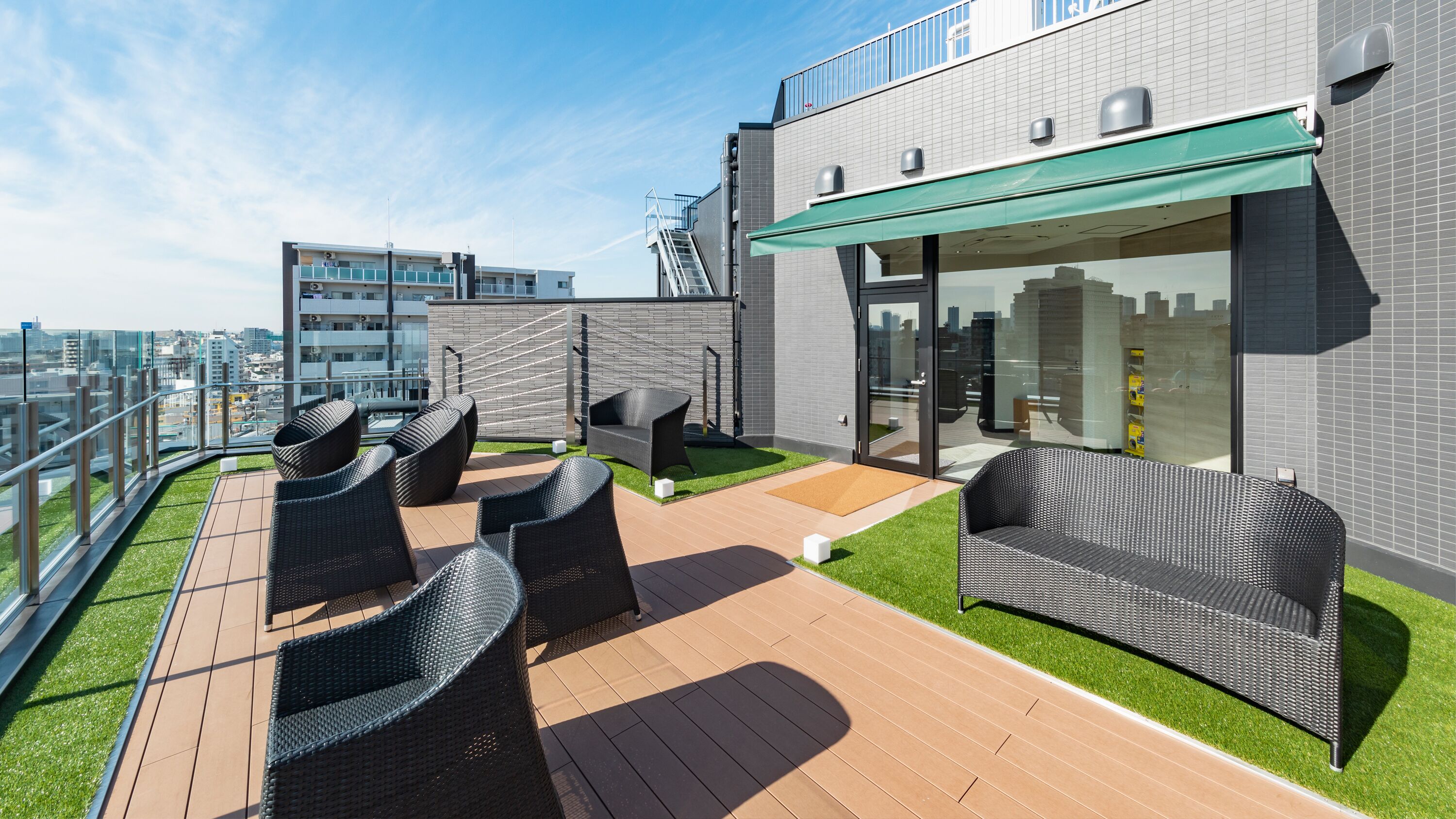 Una terraza en la azotea con mobiliario exterior, un cerramiento de vidrio y vistas a la ciudad.