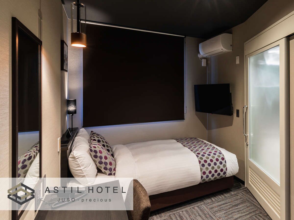 A hotel room with a bed, a TV mounted on the wall, a window with frosted glass, and a wall-mounted air conditioning unit.