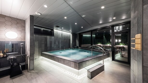 A modern bathroom with a large rectangular bathtub, a glass-enclosed shower area, and a vanity with a mirror and sink. - Astil Hotel Juso Precious (Osaka)