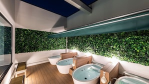 A modern spa area with wooden flooring, multiple hot tubs, and a green wall with foliage. - Astil Hotel Juso Precious (Osaka)