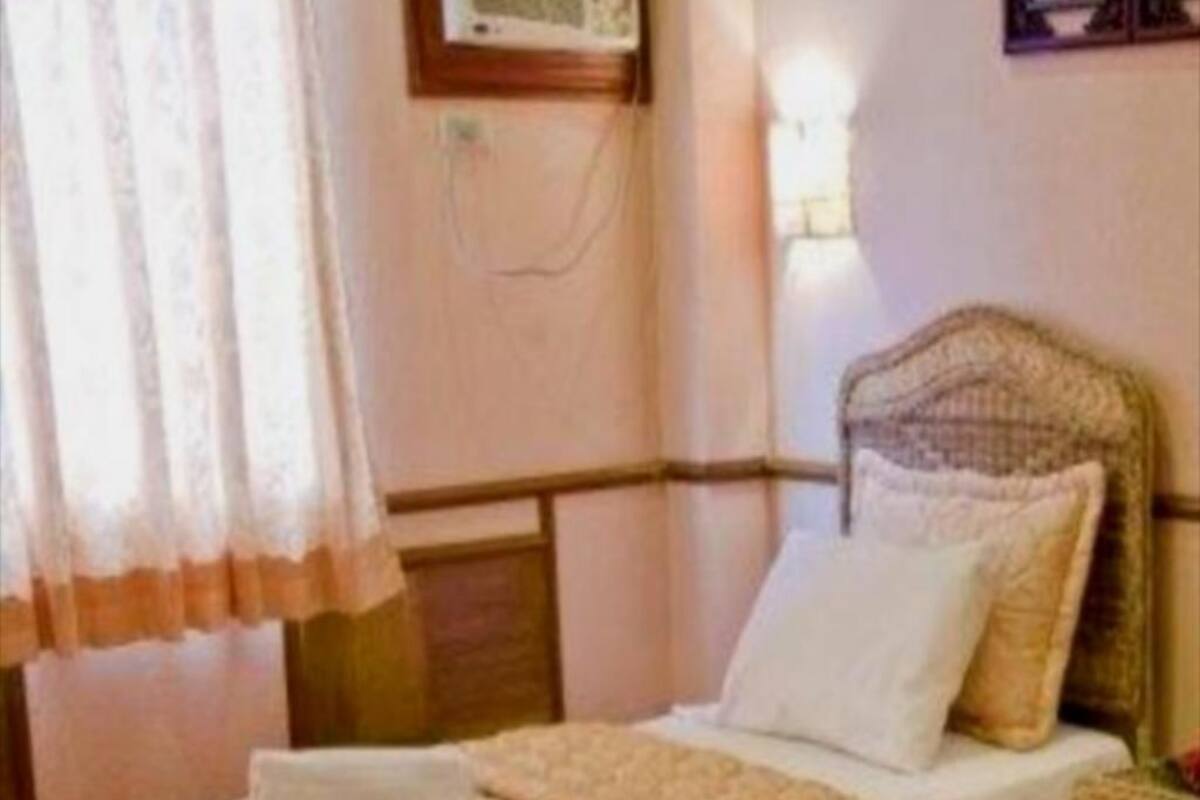 A bedroom with a wooden headboard, a bed with a beige blanket, a white pillow, and a nightstand with a lamp.