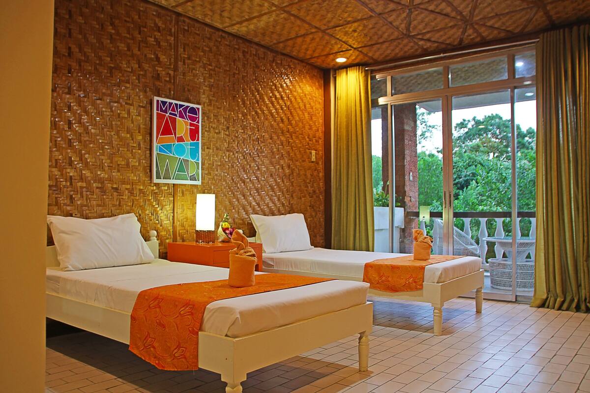 A hotel room with two beds, a wooden wall, a balcony with a view of greenery, and a sign on the wall.