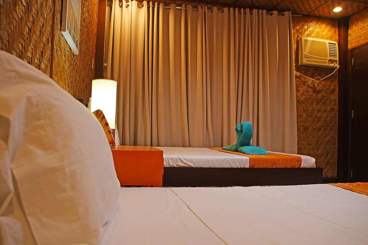 A hotel room with a bed, a nightstand, a lamp, and a window with curtains.