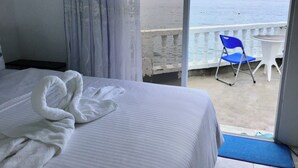 Ett hotellrum med en säng, en vit handduk, en balkong med en blå stol och utsikt över havet.