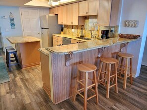 A kitchen with wooden cabinets, a built-in island with stools, a refrigerator, and a coffee maker.