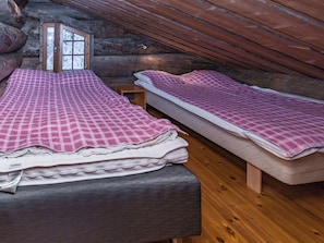 Acogedora habitación de cabaña de troncos con una cama en un entrepiso, una cama más pequeña y una ventana con vistas a la nieve.