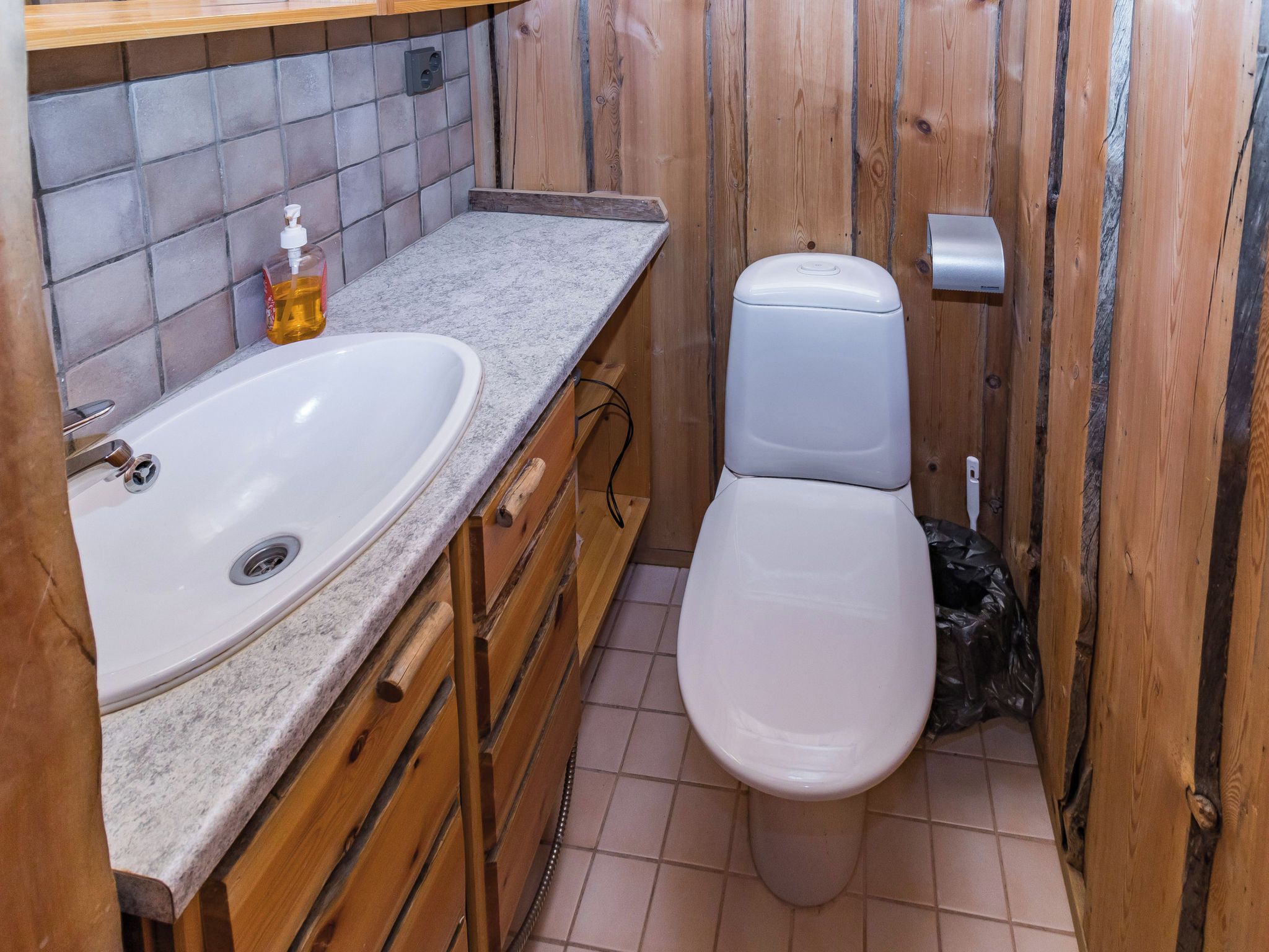 Een kleine badkamer met een wit wastafelmeubel, houten kasten en een toilet.