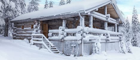 En timmerstuga med ett snötäckt tak, träfasad och en trappa som leder upp till entrén.