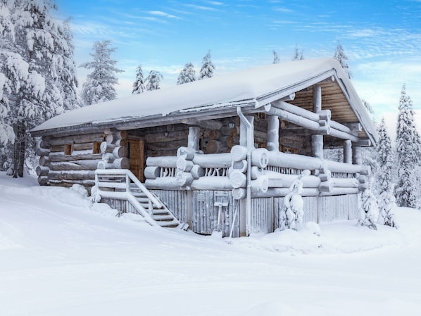 A log cabin with a snow-covered roof, wooden exterior, and a staircase leading to the entrance.