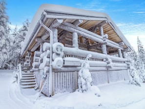 Una cabaña de troncos con techo a dos aguas, rodeada de árboles cubiertos de nieve.