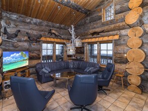 A log cabin interior with a large television, leather seating, and a wooden ceiling.