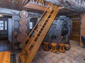 A rustic interior with a wooden staircase, a stone fireplace, and a wooden wall adorned with tree rings. - Kitka-nokkela by Interhome (Kuusamo)