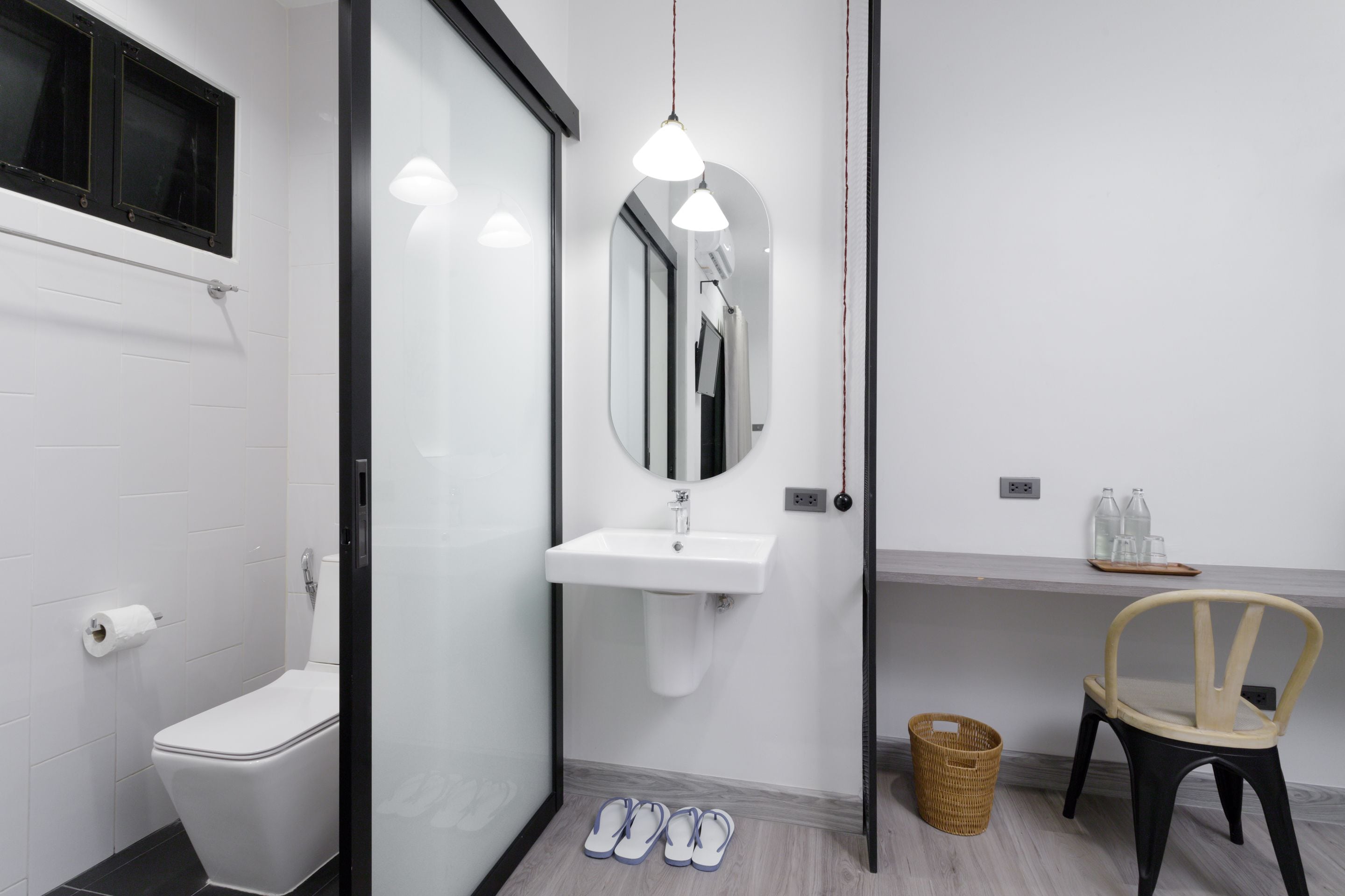A modern bathroom with a toilet, sink, mirror, and a chair.