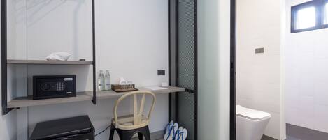 Habitación compacta con kitchenette, una silla, una mesita, microondas, refrigerador, basurero, ventana y un inodoro.