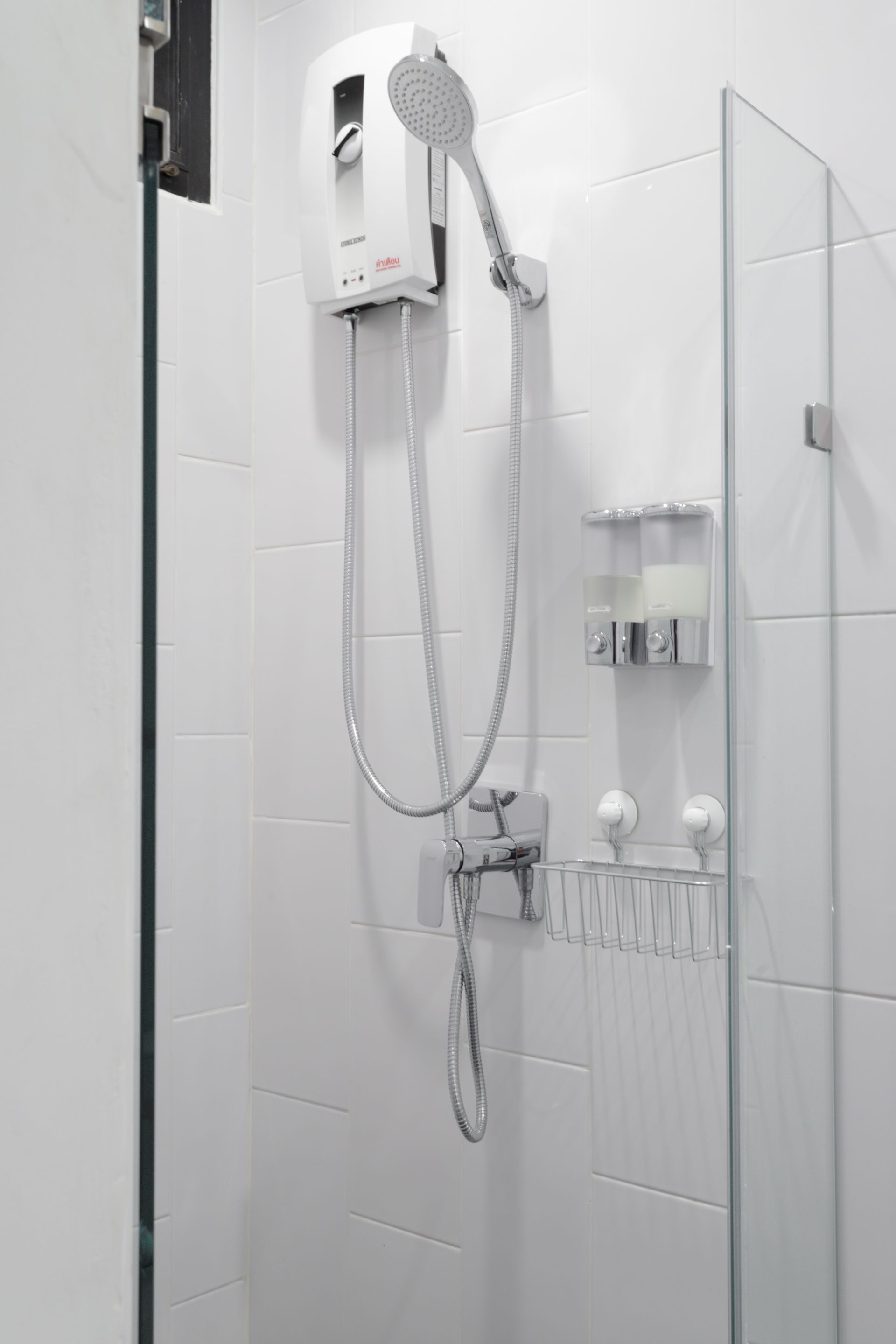 A modern bathroom with a glass shower enclosure, a handheld showerhead, and a wall-mounted control panel.