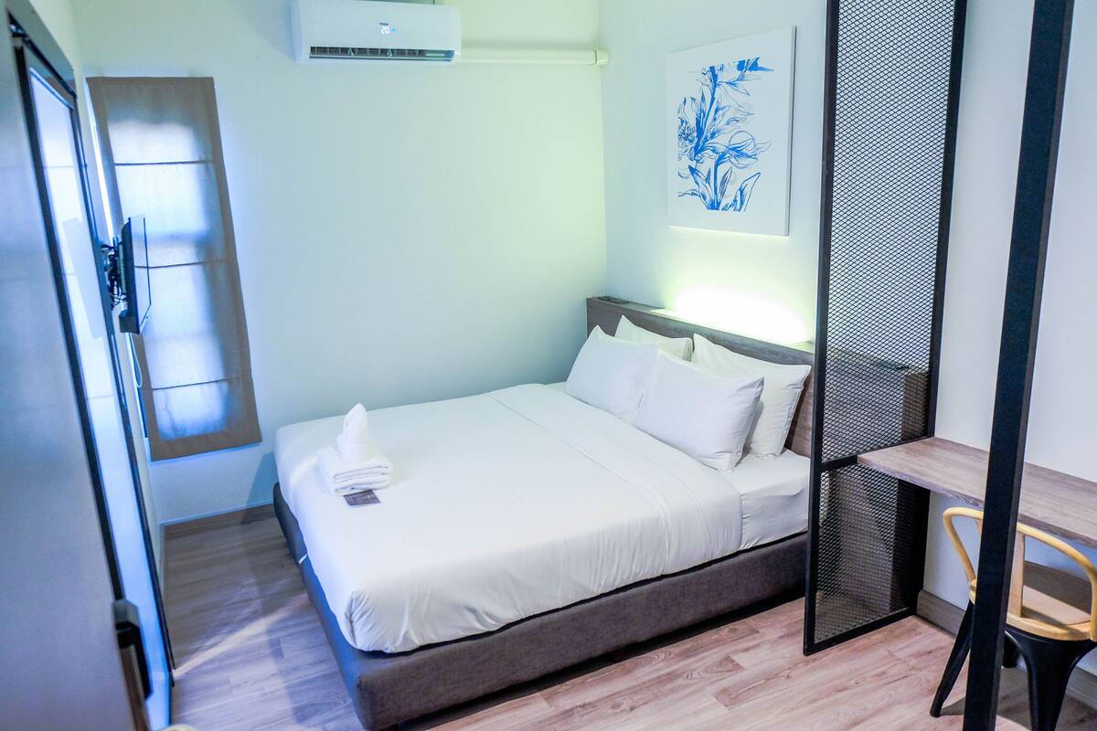 A hotel room with a bed, a desk, a chair, and a wall-mounted air conditioner.