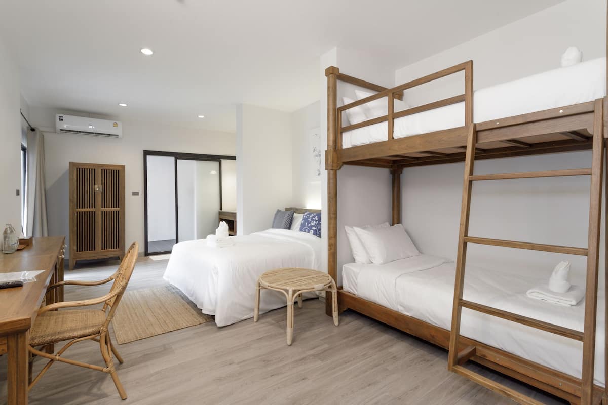 A hotel room with bunk beds, a wooden desk, a wicker chair, and a bedside table.